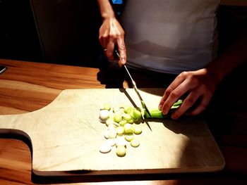 High angle view of man chopping scallion on cutting board in kitchen