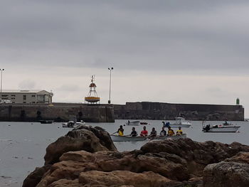 People on rocks by sea against sky