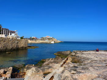 Scenic view of sea by buildings against clear blue sky