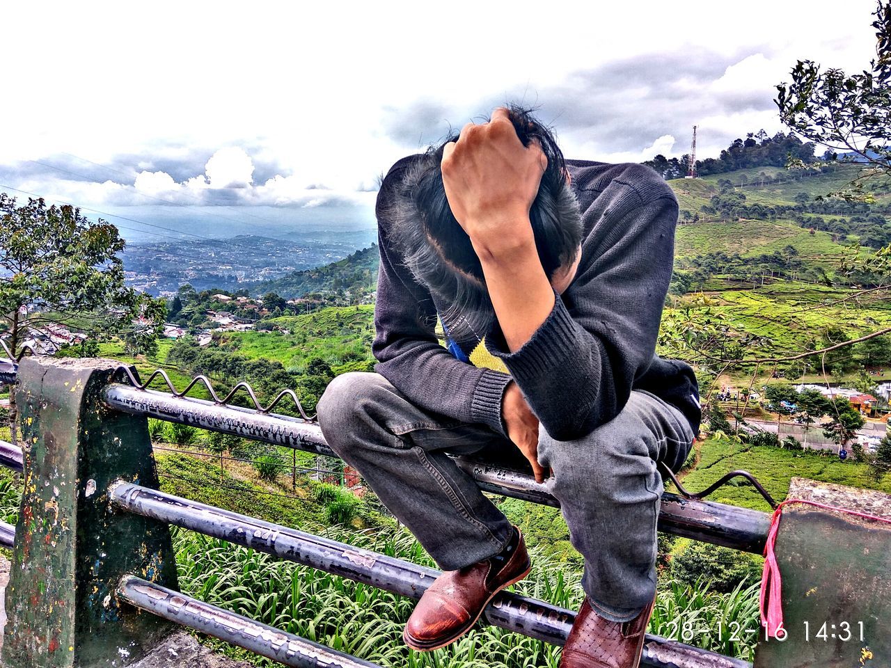 REAR VIEW OF MAN SITTING ON TERRACE AGAINST CITYSCAPE