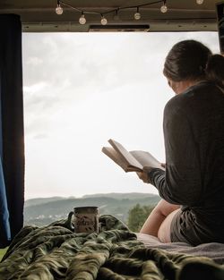 Rear view of woman reading book sitting against sky