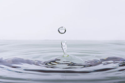 Close-up of drop falling on water against white background