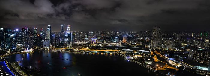 Illuminated buildings by river against sky at night