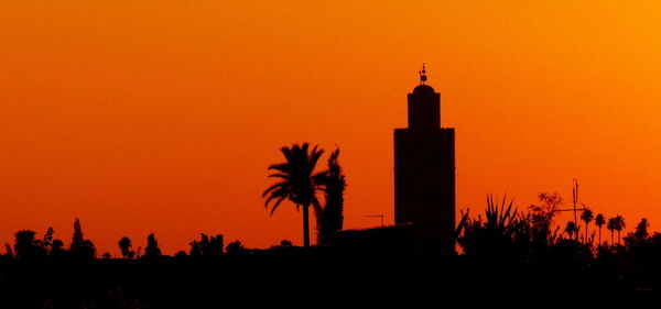 Silhouette trees and buildings against orange sky