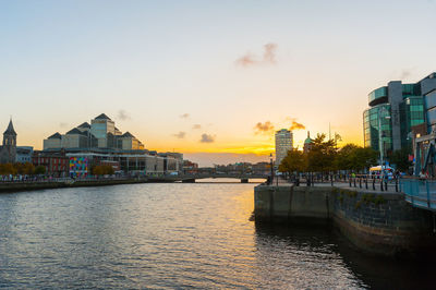 River by buildings against sky during sunset
