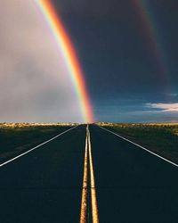 Rainbow over road against sky
