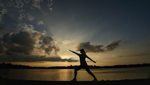 Silhouette person standing by sea against sky during sunset