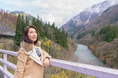 Portrait of beautiful woman standing by railing against mountains