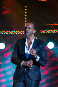 Singer wearing suit standing on illuminated stage at event