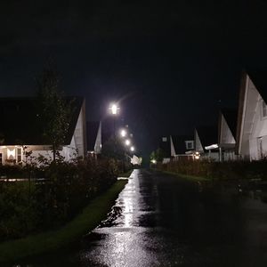 Illuminated street amidst buildings against sky at night