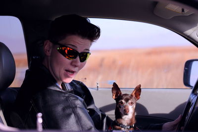 Portrait of young woman with dog sitting in car