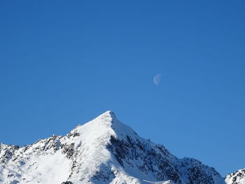 Low angle view of snowcapped mountains against clear blue sky