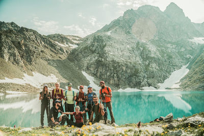 People standing by lake against mountains