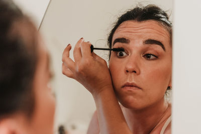 Mirror photo of beautiful young woman putting on makeup