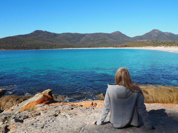 Rear view of woman sitting against sea and mountains