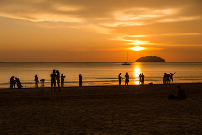 Silhouette people on beach against sky during sunset