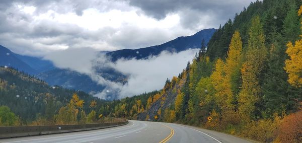 Road amidst trees and mountains against sky