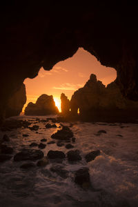 Silhouette rock formation in sea against sky during sunset