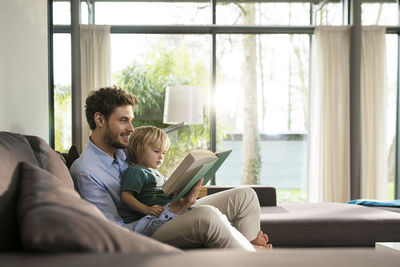 Father and son reading book on couch at home