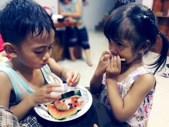 Close-up of siblings eating watermelon in plate at home