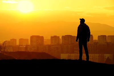Rear view of silhouette man standing on mountain during sunset