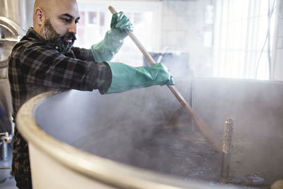 Mid adult worker stirring beer in container while working at brewery