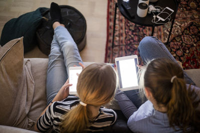 High angle view of sisters using wireless technologies while sitting on sofa at home