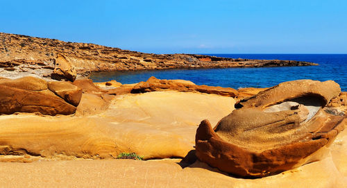 Rock formations on shore against clear blue sky