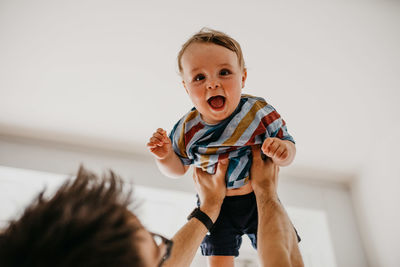 Portrait of cheerful baby boy carried by father at home