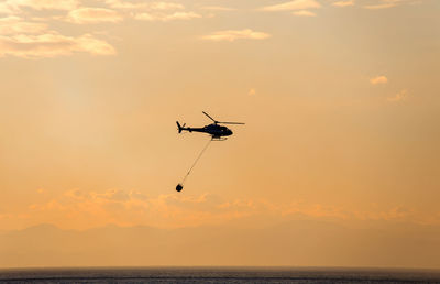 Silhouette helicopter in sea against sky during sunset