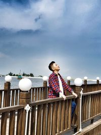 Man standing by railing against sky