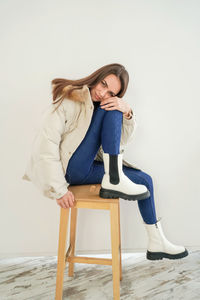 Young woman sitting on chair against white background