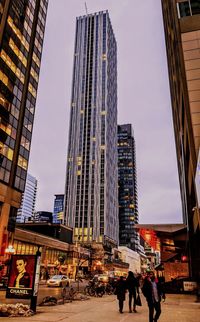 People on street by modern buildings against sky in city