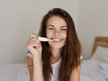 Portrait of smiling woman holding thermometer on bed