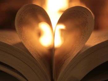 Close-up of heart shape made up from book pages against fireplace