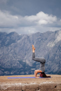 Side view full length of woman exercising on cliff against mountain