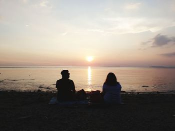 Rear view of couple sitting on beach at sunset