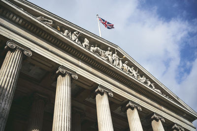 From below flag of great britain fluttering on top of aged ornamental building with columns against cloudy sky