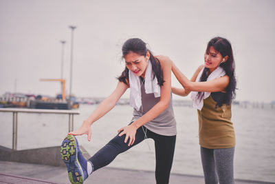 Woman assisting friend in exercising at beach
