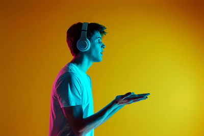 Rear view of woman with arms raised standing against yellow wall