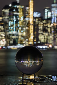 Close-up of illuminated glass with reflection on city at night