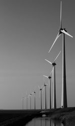 Windmills in row on field against sky