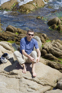 Portrait of young man sitting on rocks against lake