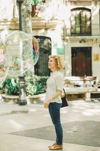 Woman standing by huge bubbles on footpath in city