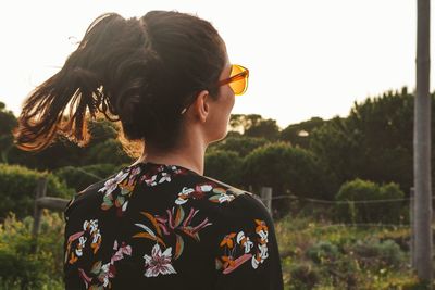 Young woman wearing sunglasses looking away while standing against sky