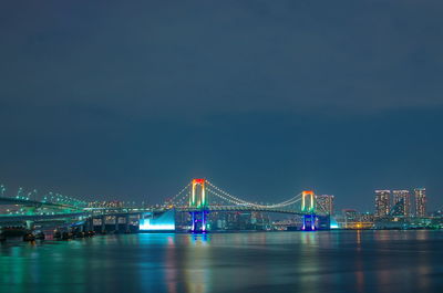 Illuminated bridge over river with city in background