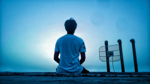 Rear view of men sitting against blue sky