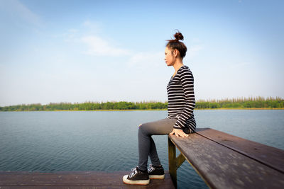 Young woman sitting on lake against sky