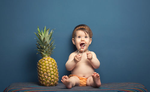 Portrait of shirtless boy holding fruit against blue sky