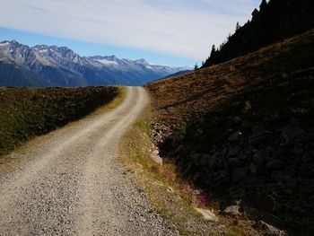 Dirt road by mountains against sky